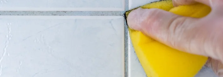 Hand reinigt Fliesenfugen mit Schwamm